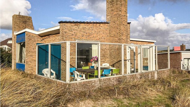 Una casa moderna con un porche de vidrio, paredes de ladrillo y dos chimeneas.