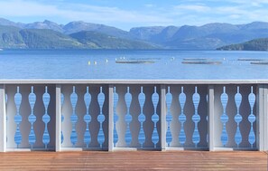 Une terrasse en bois agrémentée d’une balustrade décorative, donnant sur un lac paisible avec des montagnes en arrière-plan.