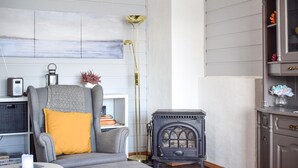 Una sala de estar acogedora con un sofá gris, una lámpara de pie alta, una estufa antigua y una estantería.