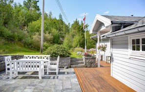 A wooden deck with white benches, a stone wall, and a white building with a sloped roof. - 3 bedroom beach front home in Jondal (Jondal)
