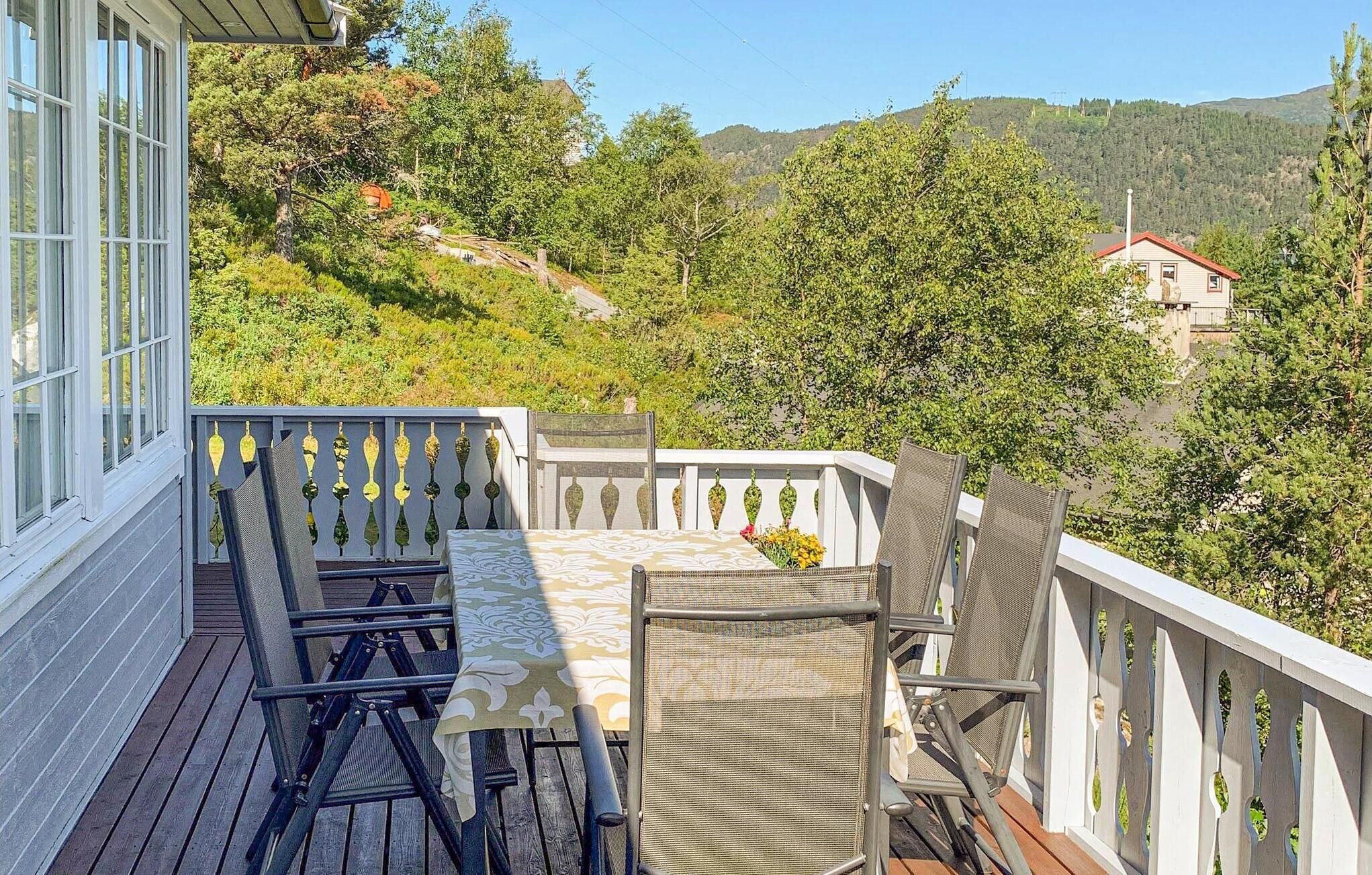 A balcony with a table and chairs, overlooking a mountainous landscape.