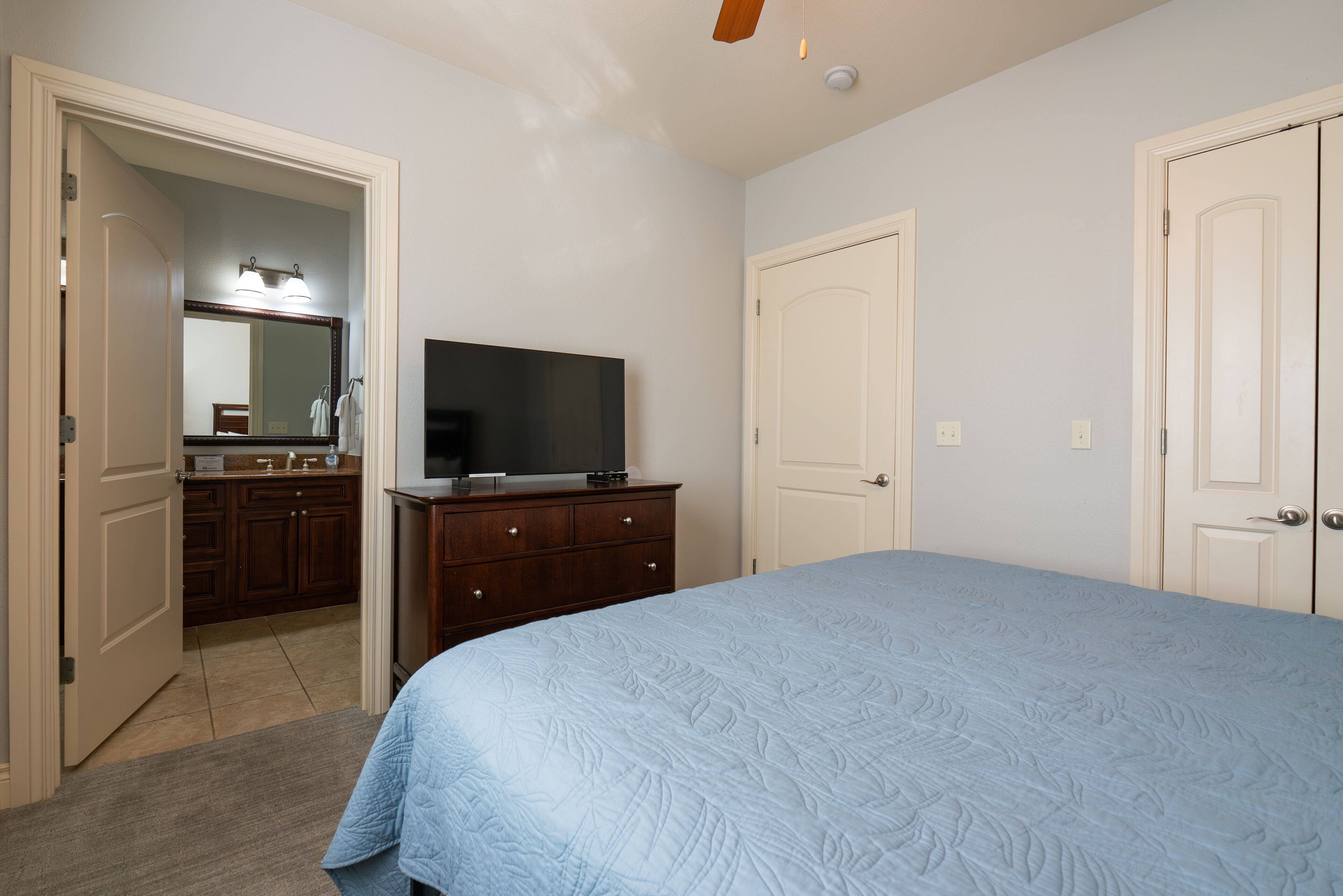 A bedroom with a bed, a dresser, a television, and a door.