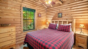 Ein Schlafzimmer in einer Blockhütte mit Bett, Kommode, Fenster und Deckenventilator.