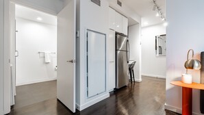 A modern kitchen with a stainless steel refrigerator, a dining area with a table and chairs, and a hallway leading to another room. - Studio | Gym, Pool | Bellevue | Sophari Towers A (Bellevue)
