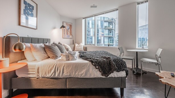 A modern bedroom with a large bed, a desk, and a window with a city view. - Studio | Gym, Pool | Bellevue | Sophari Towers A (Bellevue)