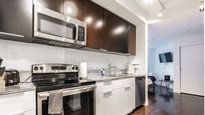A modern kitchen with a microwave, stove, and oven, a sink, and a dining area with a TV. - Studio | Gym, Pool | Bellevue | Sophari Towers A (Bellevue)