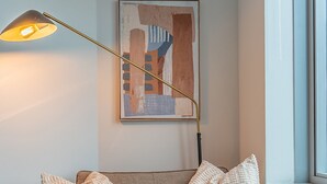 A modern living room with a sofa, ottoman, and a floor lamp. - Studio | Gym, Pool | Bellevue | Sophari Towers A (Bellevue)
