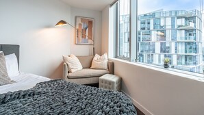 A modern bedroom with a bed, a sofa, a window with a city view, and a floor lamp. - Studio | Gym, Pool | Bellevue | Sophari Towers A (Bellevue)