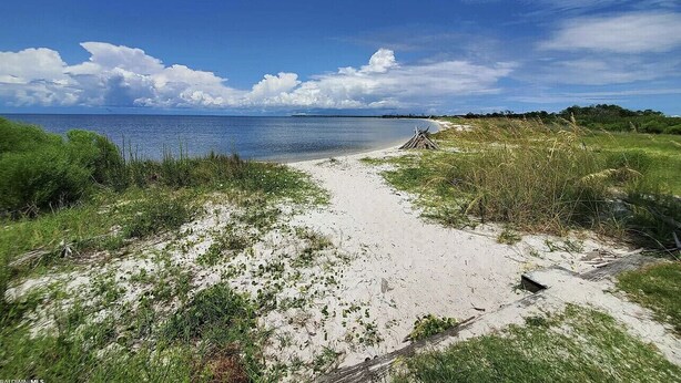 Ein Strandweg führt zum Wasser, der Himmel ist wolkenlos.