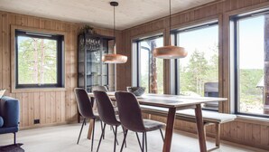 A dining area with a wooden table and chairs, large windows, and pendant lights. - Stunning home in Vatnestrøm with sauna (Vatnestrøm)