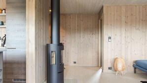A modern interior with a black wood-burning stove, wooden walls, a sofa, and a wicker chair. - Stunning home in Vatnestrøm with sauna (Vatnestrøm)