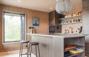 Una cucina moderna con rivestimenti in legno, un'isola grande con sgabelli, una lampada a sospensione e vista sull'esterno.