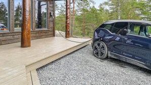 A modern wooden cabin with a deck, a car parked in front, and a forested backdrop. - Stunning home in Vatnestrøm with sauna (Vatnestrøm)