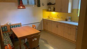 Kompakti keittiö, jossa on puiset kaapit, ruokapöytä tuoleineen ja ikkuna, jossa on verhot.