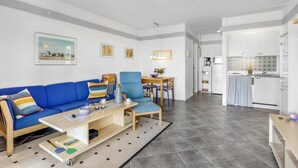 A modern living room with a blue sofa, a wooden coffee table, and a dining area with a blue chair and a small table. - Nice apartment in Aakirkeby (Aakirkeby)