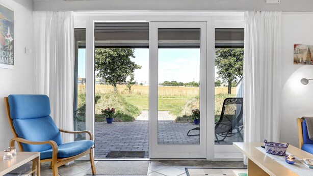A room with a blue chair, a table with a bowl and candles, and a view of a field through a glass door. - Nice apartment in Aakirkeby (Aakirkeby)