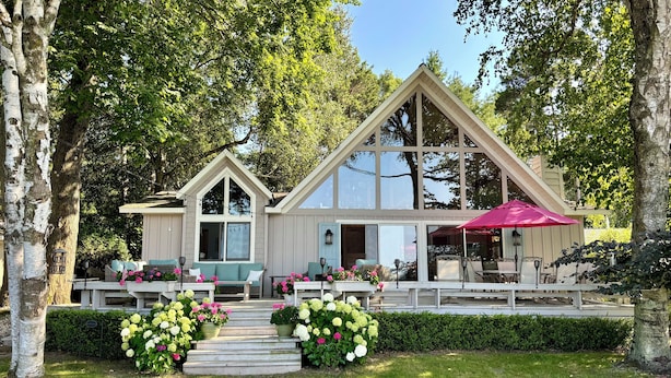A modern house with a large deck, outdoor seating, and a well-maintained garden. - Large beautiful lake front house on Silver Lake MI (Mears)