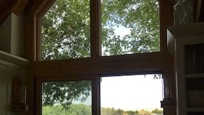 A kitchen with a large bay window overlooking a lake, a dining area with outdoor seating, and a fruit bowl on the counter. - Large beautiful lake front house on Silver Lake MI (Mears)