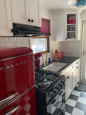 A compact kitchen with a red Galanz refrigerator, a black stove, white cabinets, and a checkered floor. - Welcome to the Lake (Northwood)