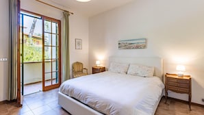 A bedroom with a large bed, two bedside tables with lamps, a chair, a painting, and a sliding glass door leading to a balcony. - Gorgeous apartment in Castiglioncello with WiFi (Castiglioncello)