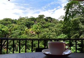 A cup on a table with a view of dense greenery and a building in the background.