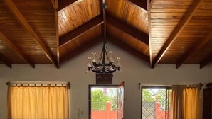 Un'ampia zona giorno con soffitto alto, un lampadario, un divano, un tavolo da pranzo con sedie e vista su un patio esterno da un'apertura.