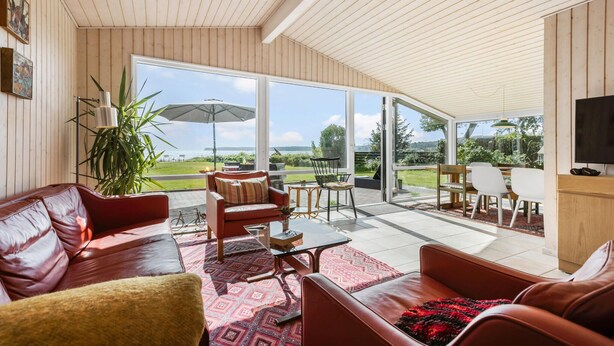 Un vaste espace de vie comprenant un canapé en cuir, une table basse et une table à manger avec des chaises. Une grande fenêtre offre une vue sur l’extérieur.