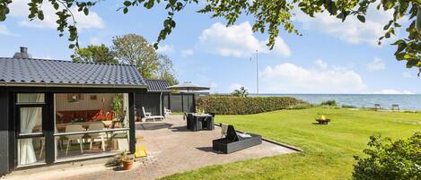 A modern house with a patio area, a dining table, and a view of the sea.
