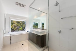 A modern bathroom with a glass shower enclosure, a window with a view, and a dual sink vanity.