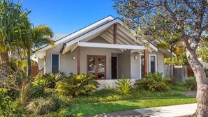 A single-story house with a front porch, surrounded by a well-maintained garden with various plants and a palm tree.