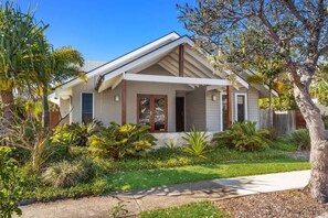 A single-story house with a front porch, surrounded by a well-maintained garden with various plants and a palm tree.