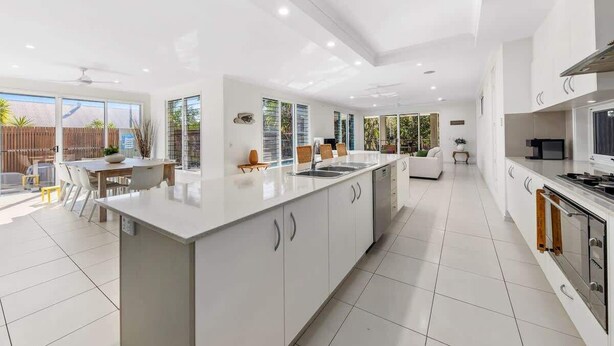 A modern kitchen with a central island, white cabinetry, and a dining area with a table and chairs.