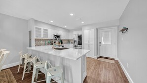 Une cuisine moderne avec des meubles blancs, un grand îlot central et un dosseret en carreaux disposés en motif chevron.