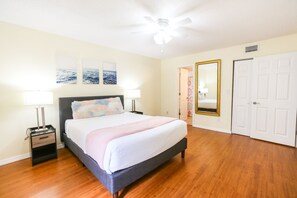 A bedroom with a bed, nightstands, a ceiling fan, and a door.