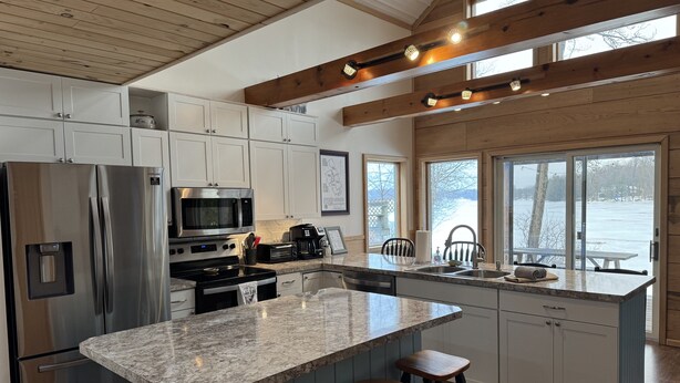 A modern kitchen with a large island, stainless steel appliances, and wooden beams. - Lakefront Cottage - Dog Friendly (Thompson)