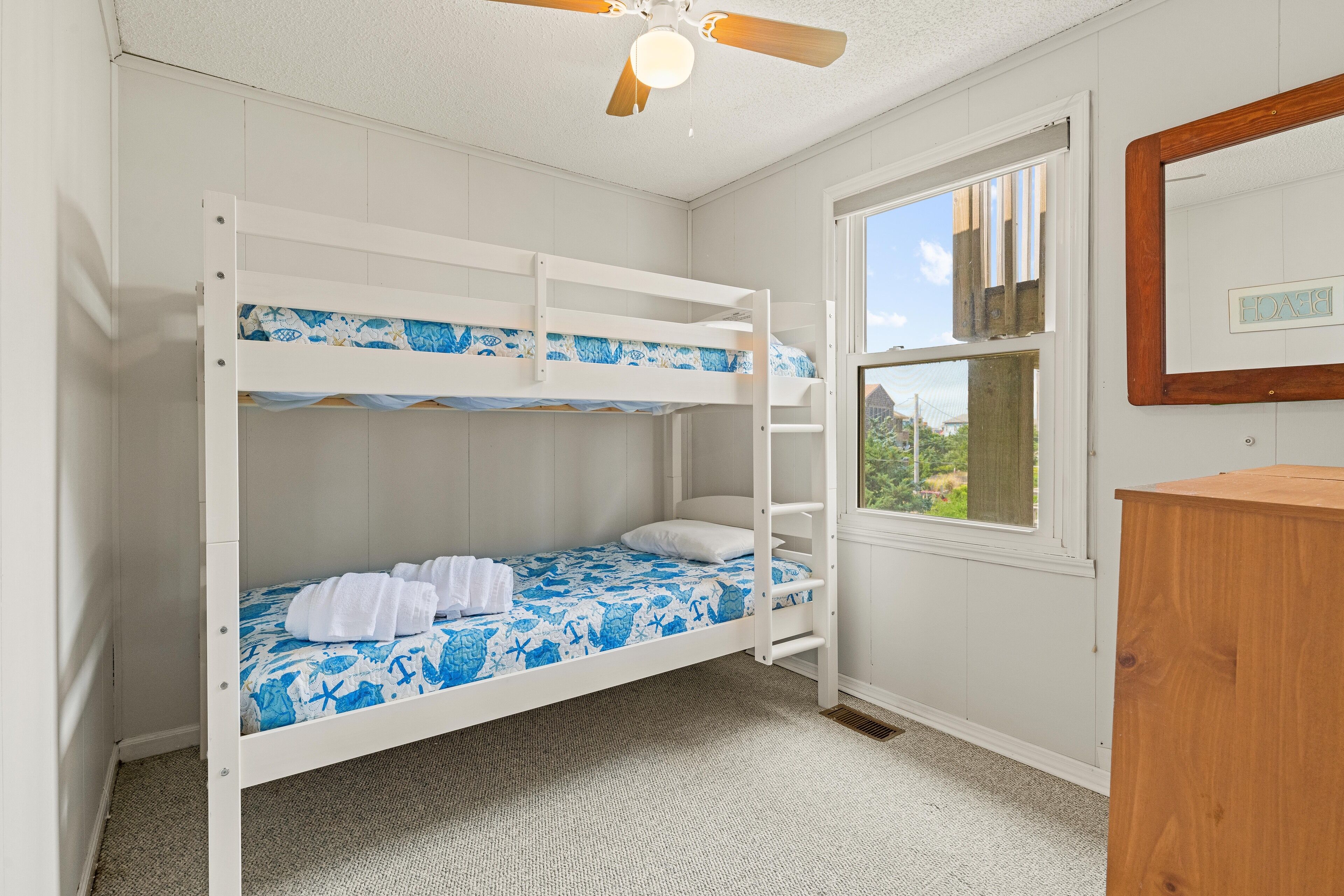 A bunk bed room with a window, a ceiling fan, and a wooden dresser.