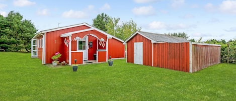 En rød lade med en hvid dør og et mindre skur ved siden af, omgivet af en grøn mark.