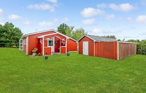 A red barn with a white door and a smaller adjacent shed, surrounded by a green field.