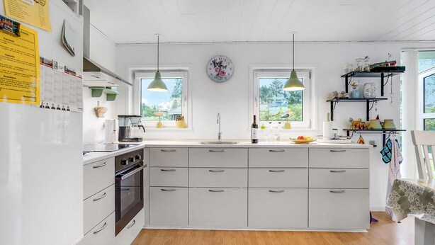 Una cocina moderna con armarios blancos, una isla central, luces colgantes y vistas a zonas verdes.