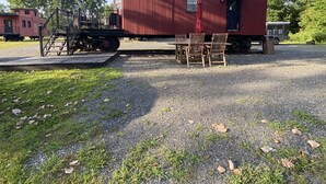 Un vagón de tren rojo transformado en edificio estacionario con zona de estar al aire libre techada.