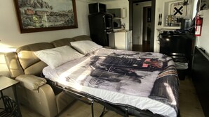 Una habitación compacta con una cama, una kitchenette pequeña, una zona de comedor y un cuadro en la pared.