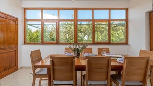 Uma sala de jantar com uma janela grande, móveis de madeira e um vaso de flores.