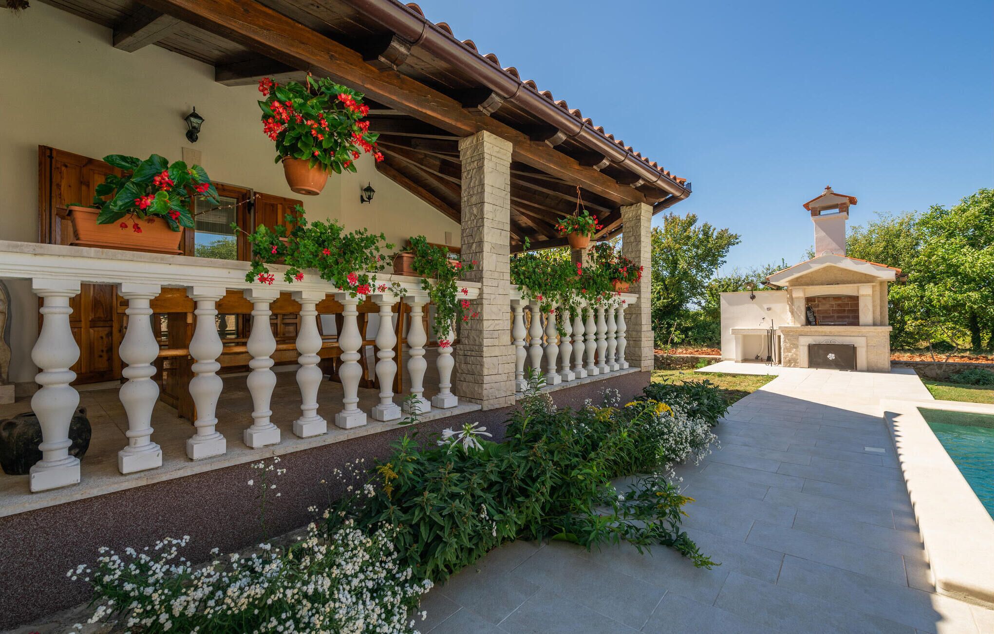 Un espace extérieur abrité, doté d’une balustrade en pierre, de plantes en pot et d’un coin barbecue.