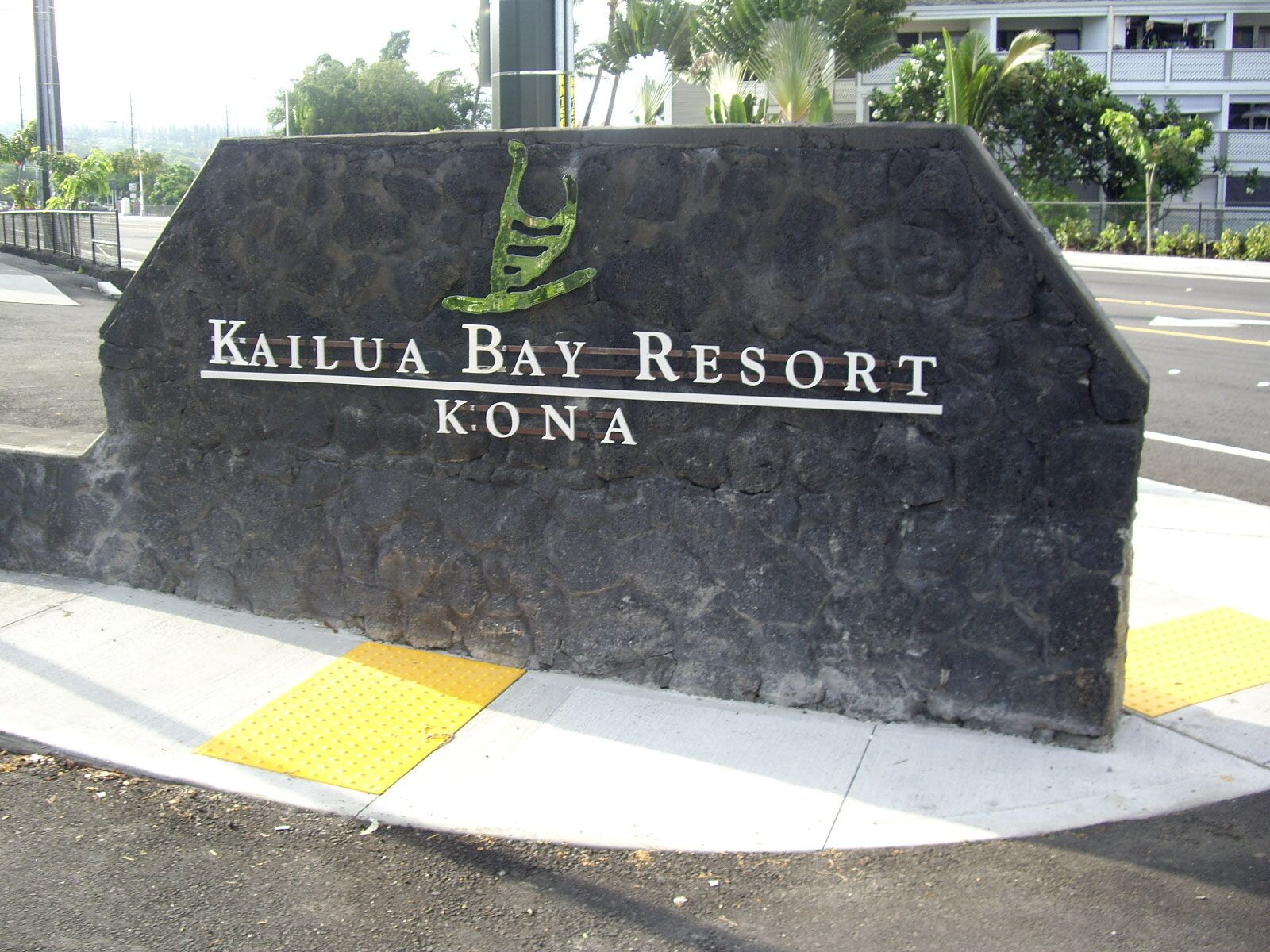 A sign for Kailua Bay Resort in Kona, featuring a stylized palm tree logo and the resort's name.