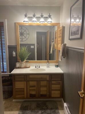 A bathroom with a large mirror, wooden cabinets, a sink, and a towel rack. - Get cozy for the winter in this 3 floor, 4 bedroom rustic ski home (Champion)