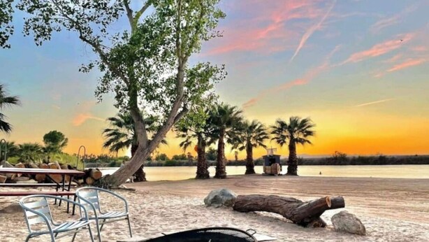 A beachside setting with a fire pit, lounge chairs, and palm trees. - Cozy 2 bedroom Cottage by the River  (Ehrenberg)