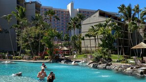 Une piscine à l’eau claire, entourée de palmiers et bordée d’un grand bâtiment doté de balcons.