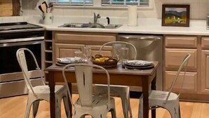 Une cuisine avec des meubles de rangement en bois, une table à manger avec des chaises et une fenêtre avec des stores.