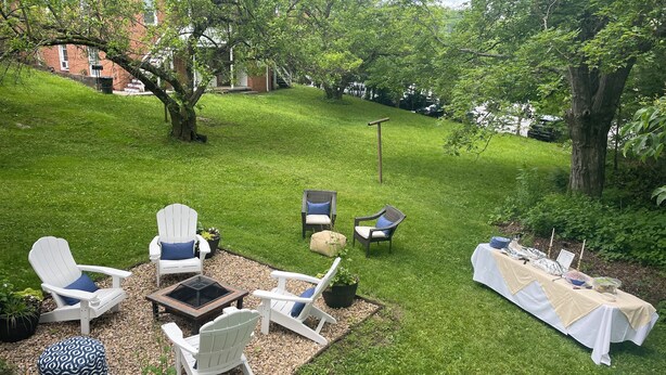 Un jardin avec un espace aménagé pour s’asseoir à l’extérieur, une table dressée pour un repas et, au fond, un bâtiment en briques.