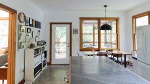 A kitchen with a central island, wooden cabinets, a clock, and a window with a view of the outdoors. - Cozy Athens Home on the Brook (Athens)